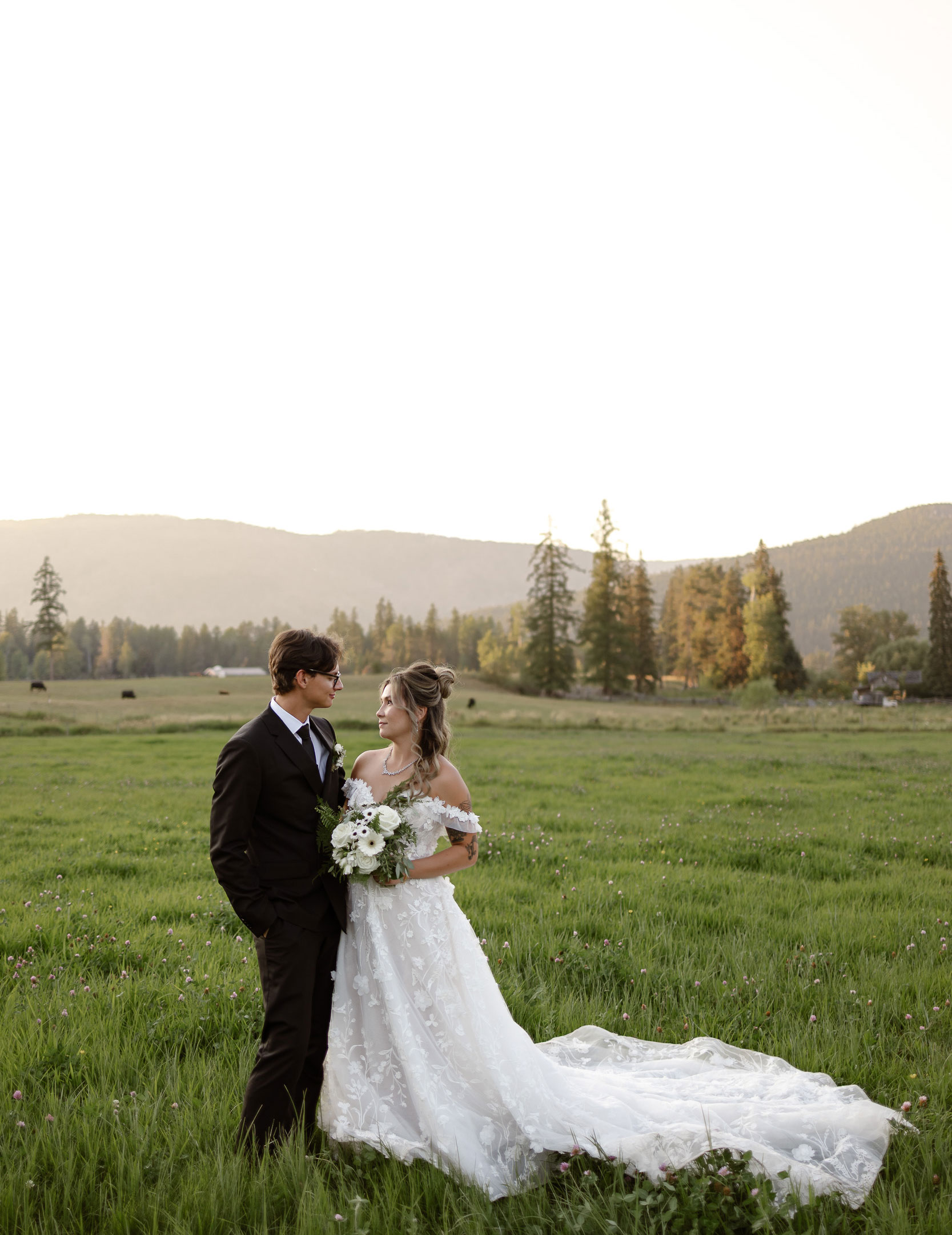 Ani and Cody share a quiet moment during their wedding portraits at Red Star Ranch in Kelowna, BC, standing in a sunlit meadow with rolling hills in the background.
