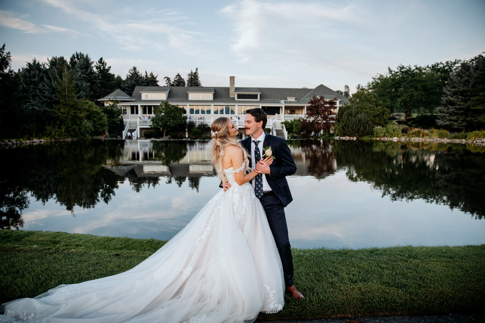 Cecilia and Kurt share a romantic moment by the lake at The Harvest Golf Club in Kelowna, BC, with the elegant clubhouse reflected in the water behind them.
