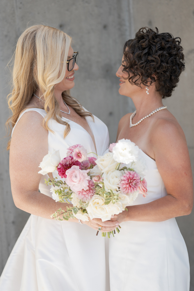 Brides Helen & Jessica sharing a joyful moment with a romantic bouquet at their Okanagan wedding at 50th Parallel Estate Winery in Lake Country, BC, planned by a professional wedding planner.