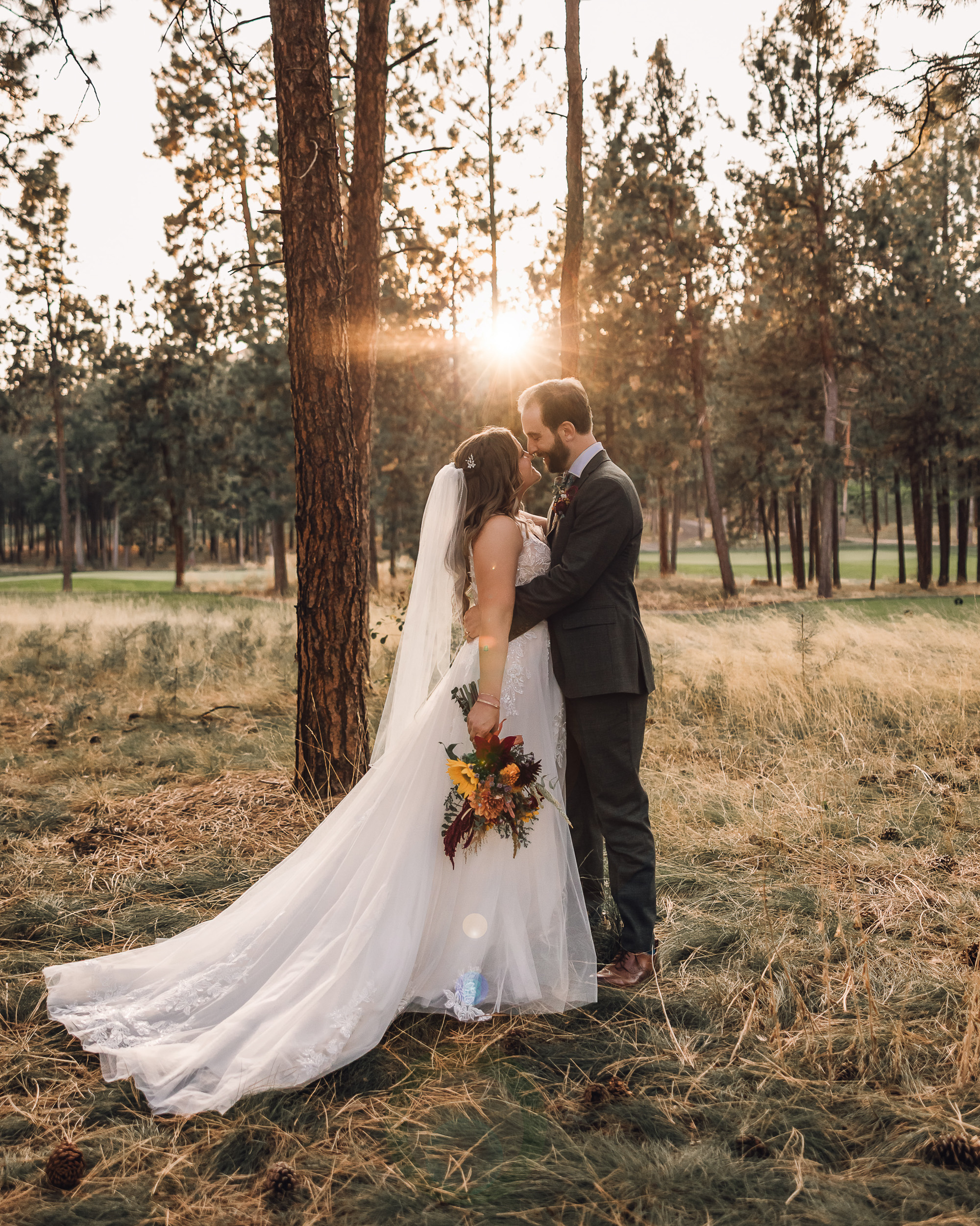 Stephanie and Phillip share a romantic embrace during their wedding portraits in Kelowna, BC, surrounded by tall pine trees and golden sunset light.